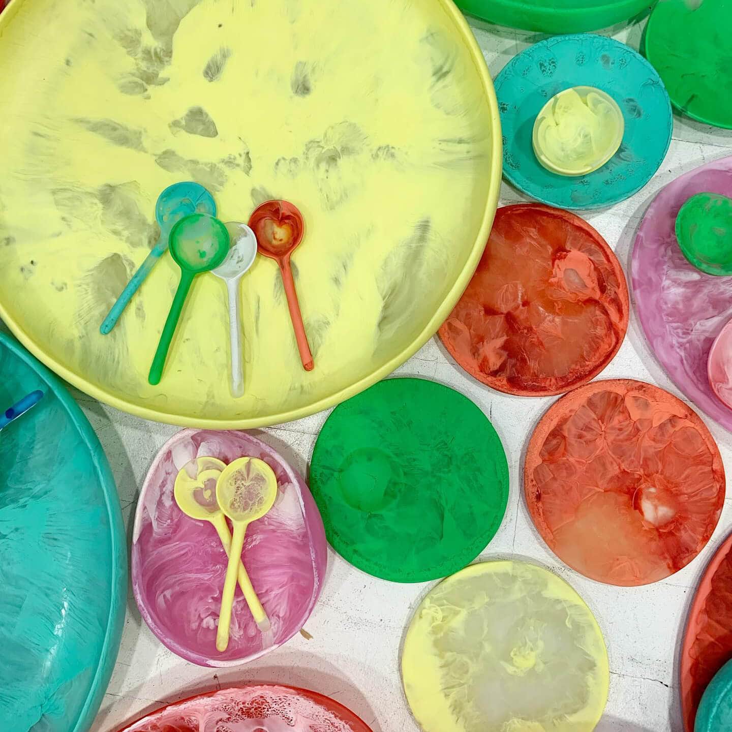 Colourful resin plates are all laid out together on a white floor.