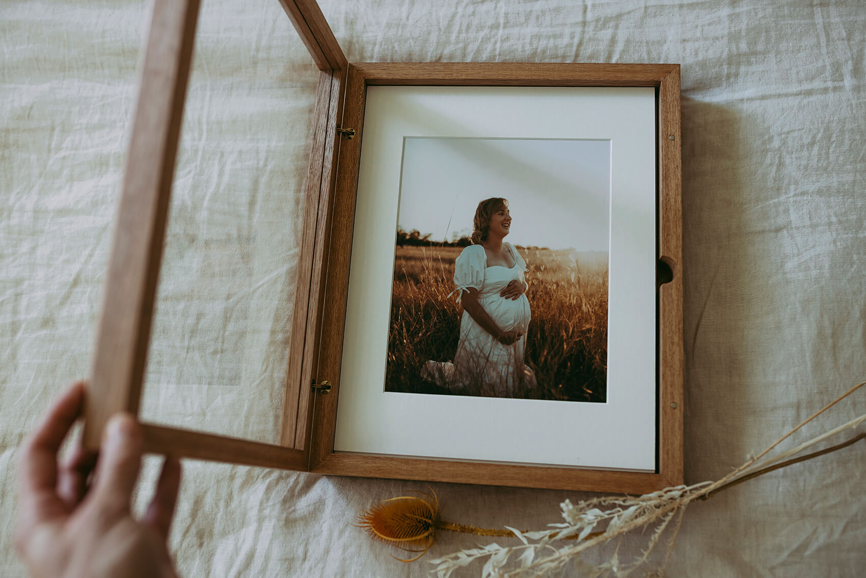 A hand in the foreground gently open a timber box. Image of a pregnant woman holding her belly inside box.