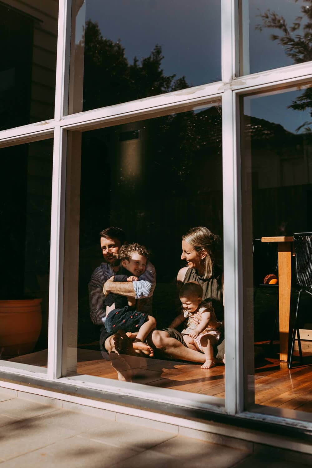 Through a big glass window, you can see a family of four cuddling.