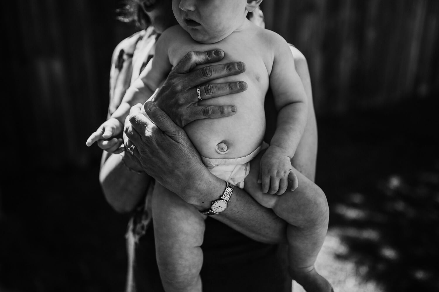 A black and white images of a woman's hands holding onto a baby. Only the babies belly is visible.