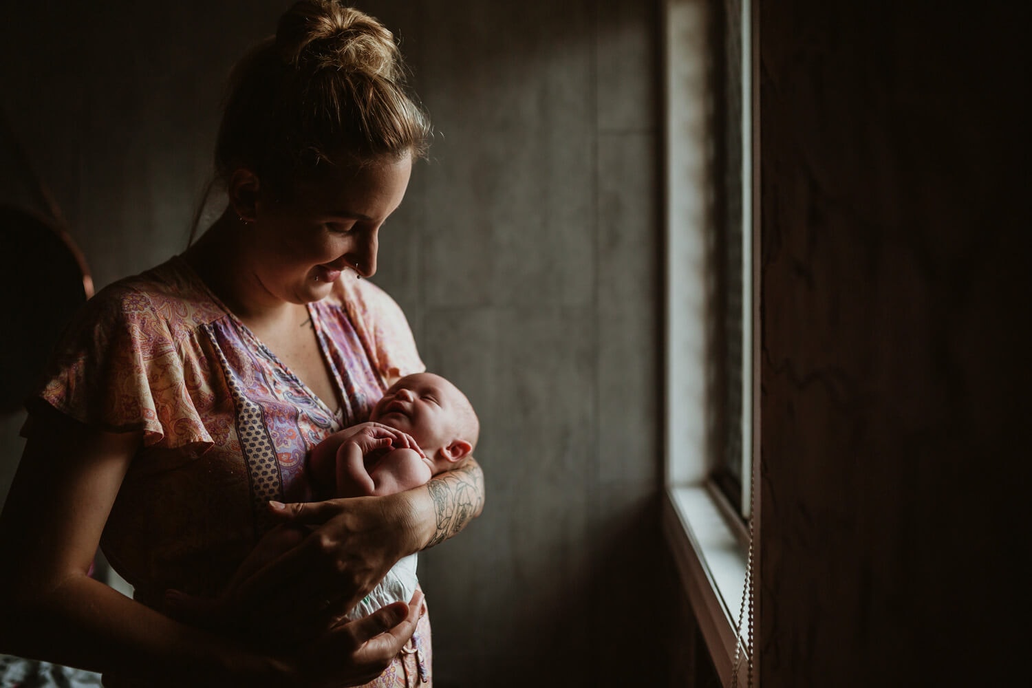 A newborn is held by its mother as light streams through the window.