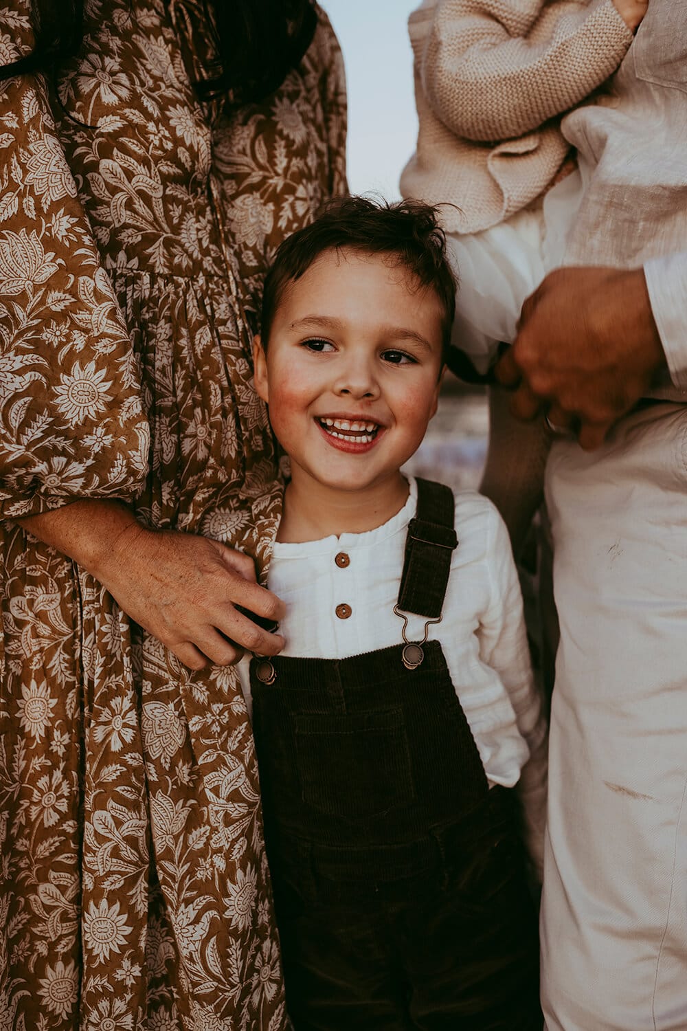 A young boy pokes his head out from between his parents with a massive smile on his face.