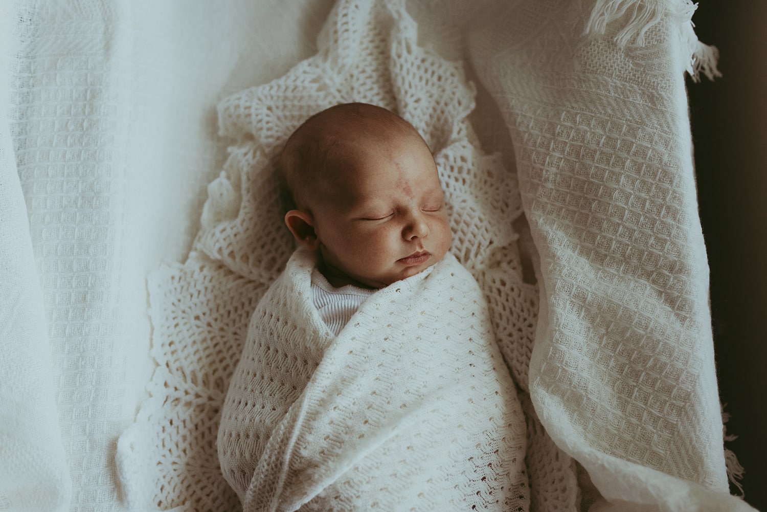 A newborn baby is wrapped in a cream heirloom blanket.