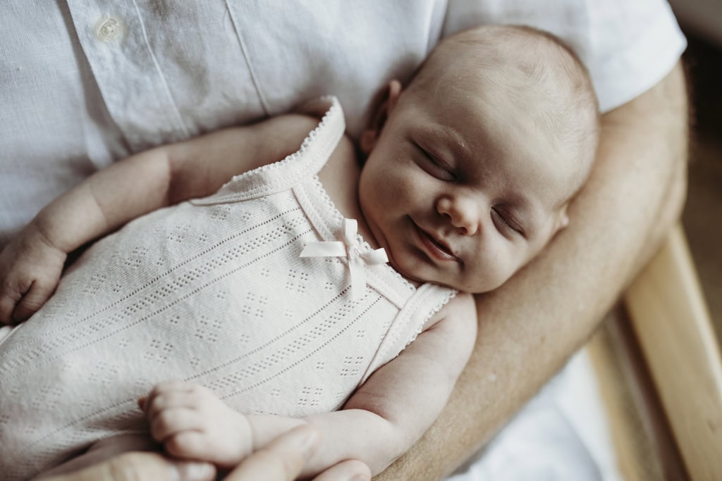 A newborn baby smiles in her sleep as she is cradled in her father's arms.