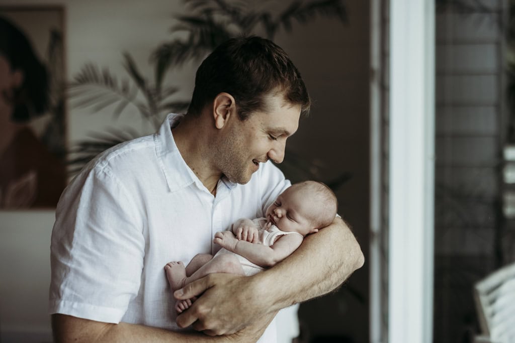 A father smiles as he cradles his newborn in his arms.