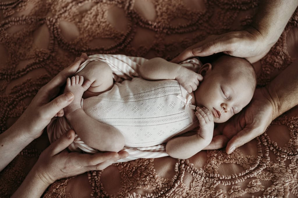 A newborn is asleep as her parents hands cradle her.