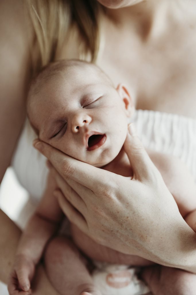 A newborn is asleep and held by her mother. The baby is sleeping with her mouth open as her mother supports her head.