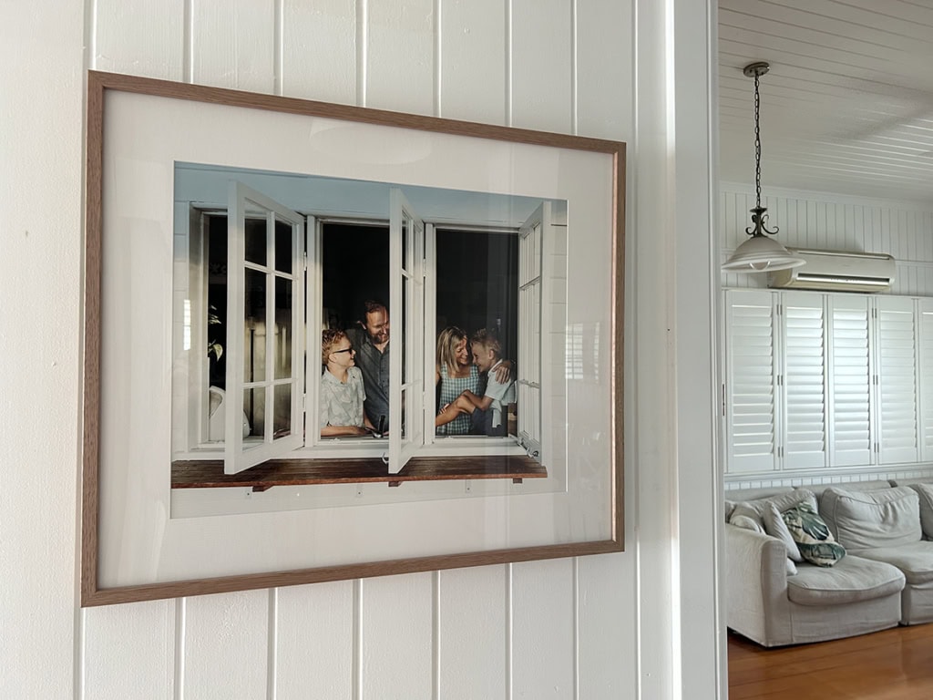 A framed family portrait hangs on the wall. The image is looking through a window at the family of four. 