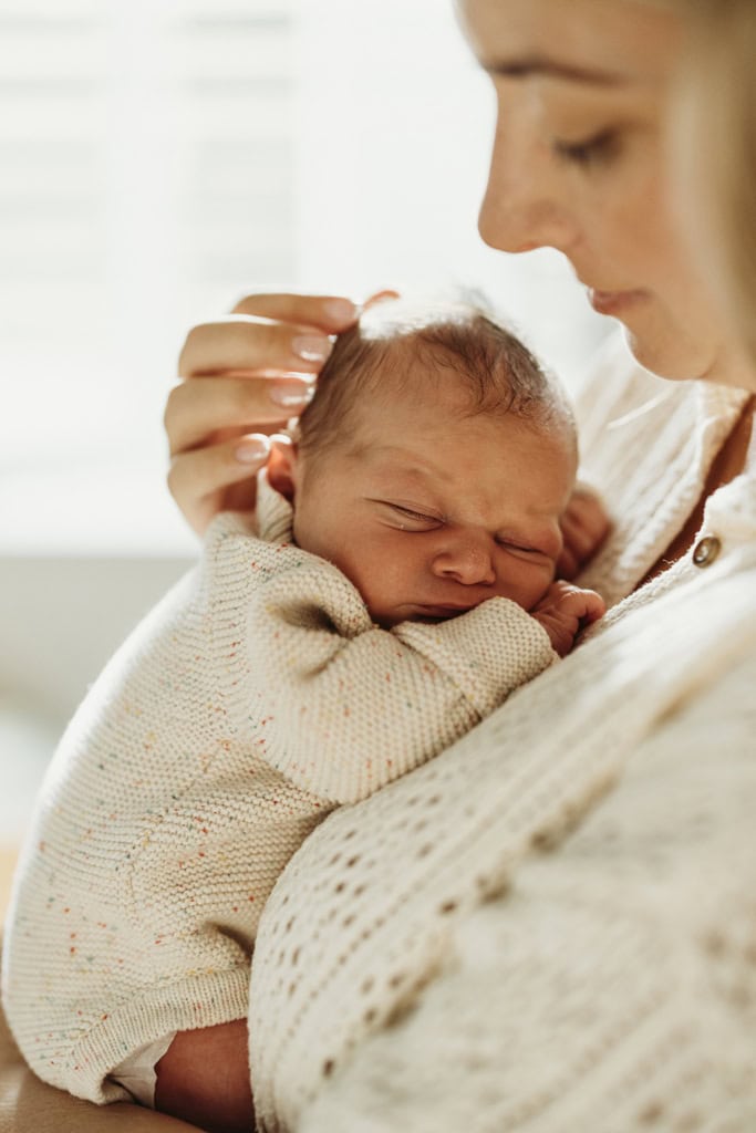 A mother cradles her baby's head as she holds him against her chest. 