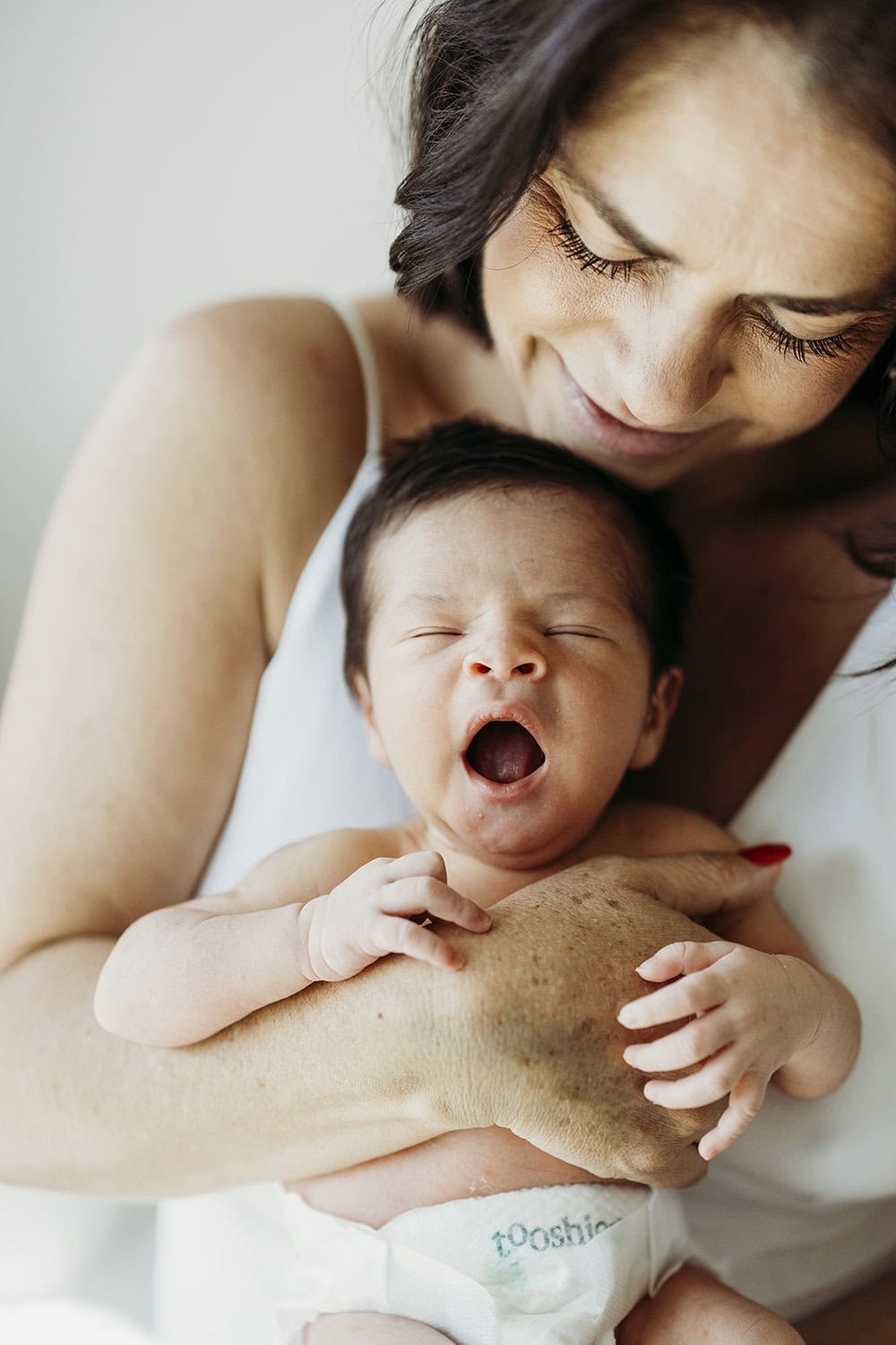 A newborn baby is held against his mother's chest as he yawns.