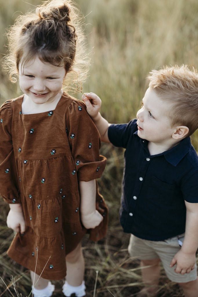 Two small children tickle each other's cheeks with grass.