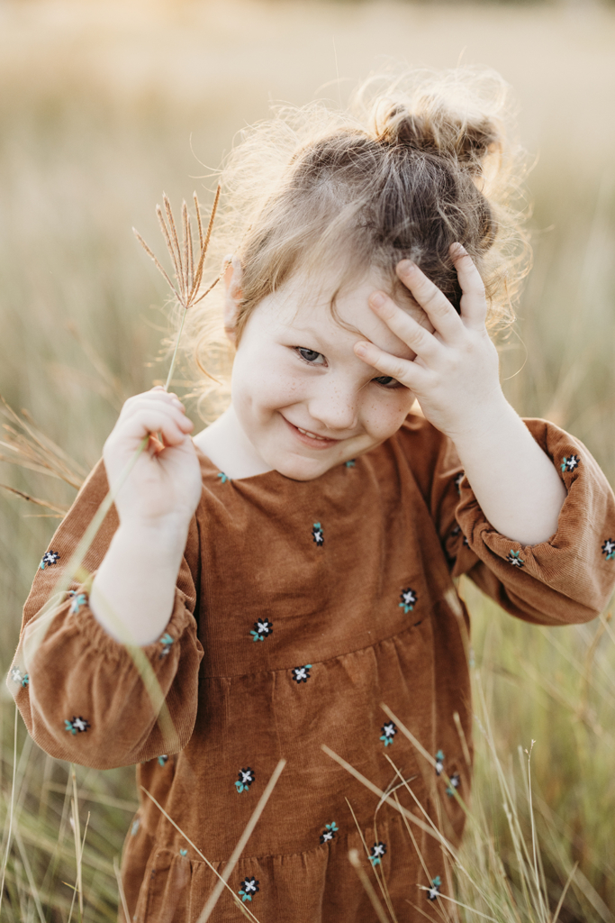 A little girl places her hand on her forehead and smiles. 