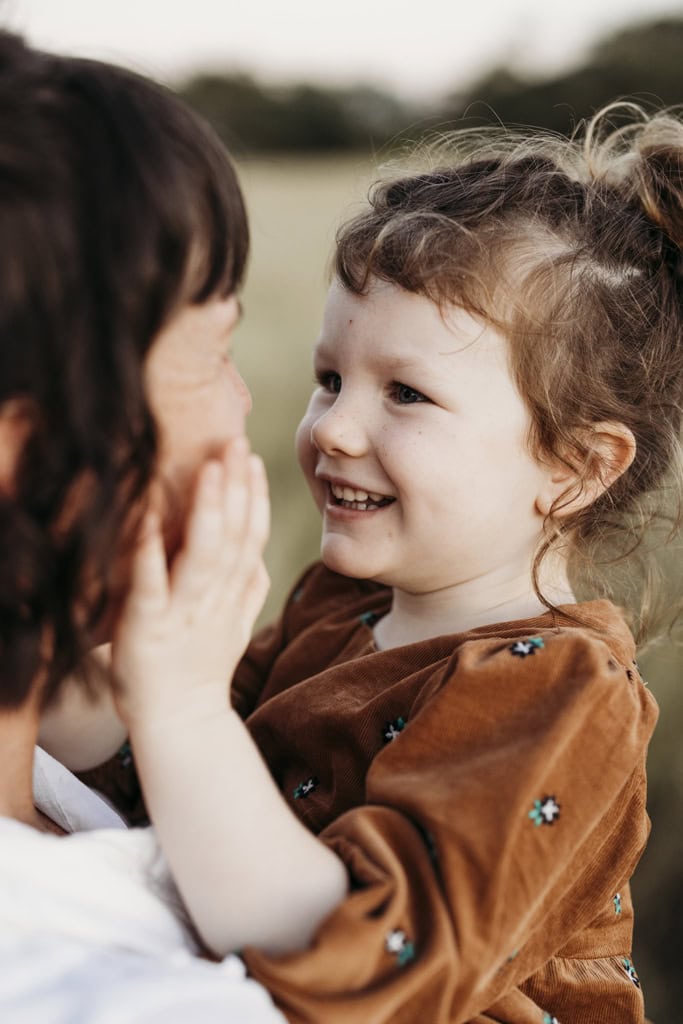 A little girl places her hands on her mother's cheeks as she smiles