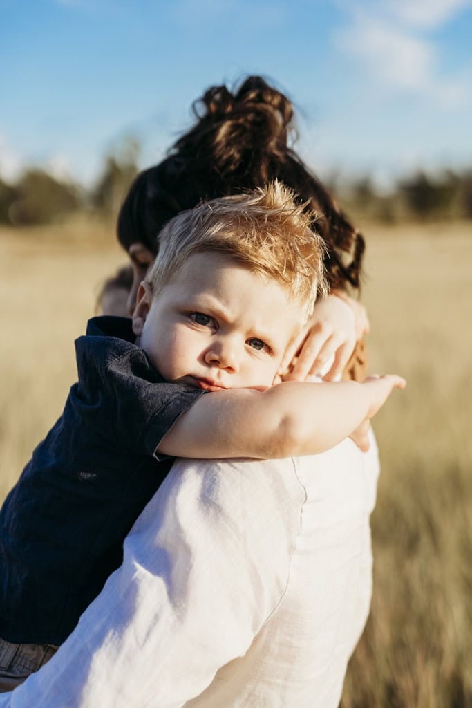 A toddler sits in his mother's arms with his arms wrapped around her neck. 