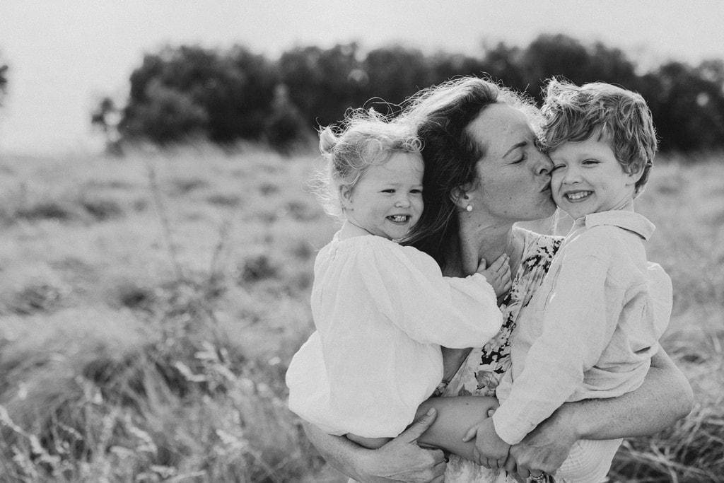 A mother kisses her son's cheeks as she holds both her children on her hips. 