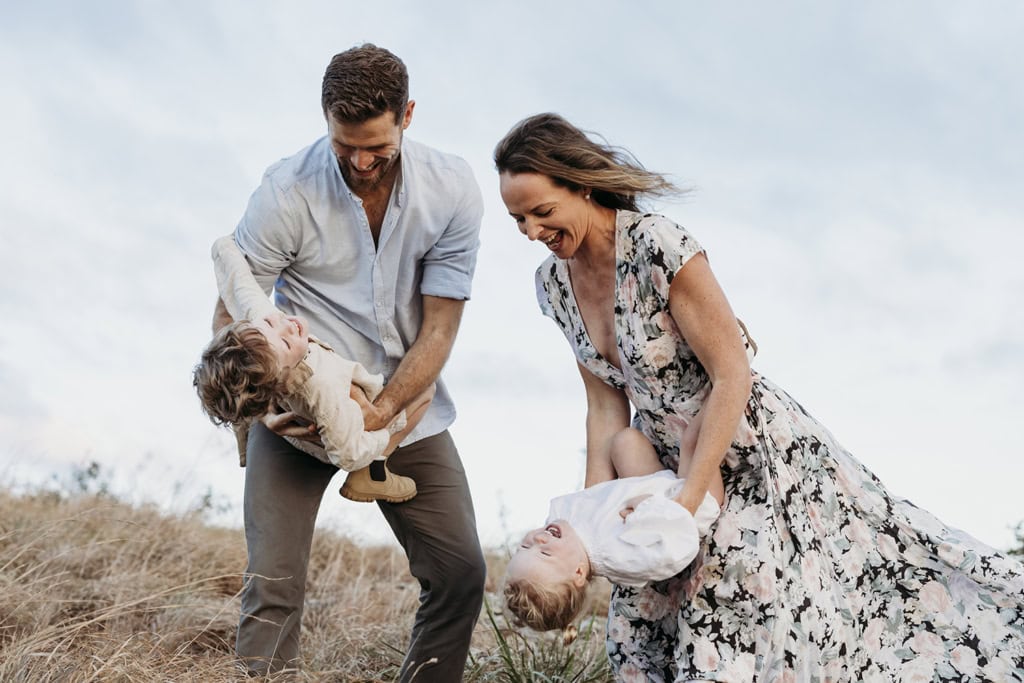 A man and woman playfully swing their children around. 