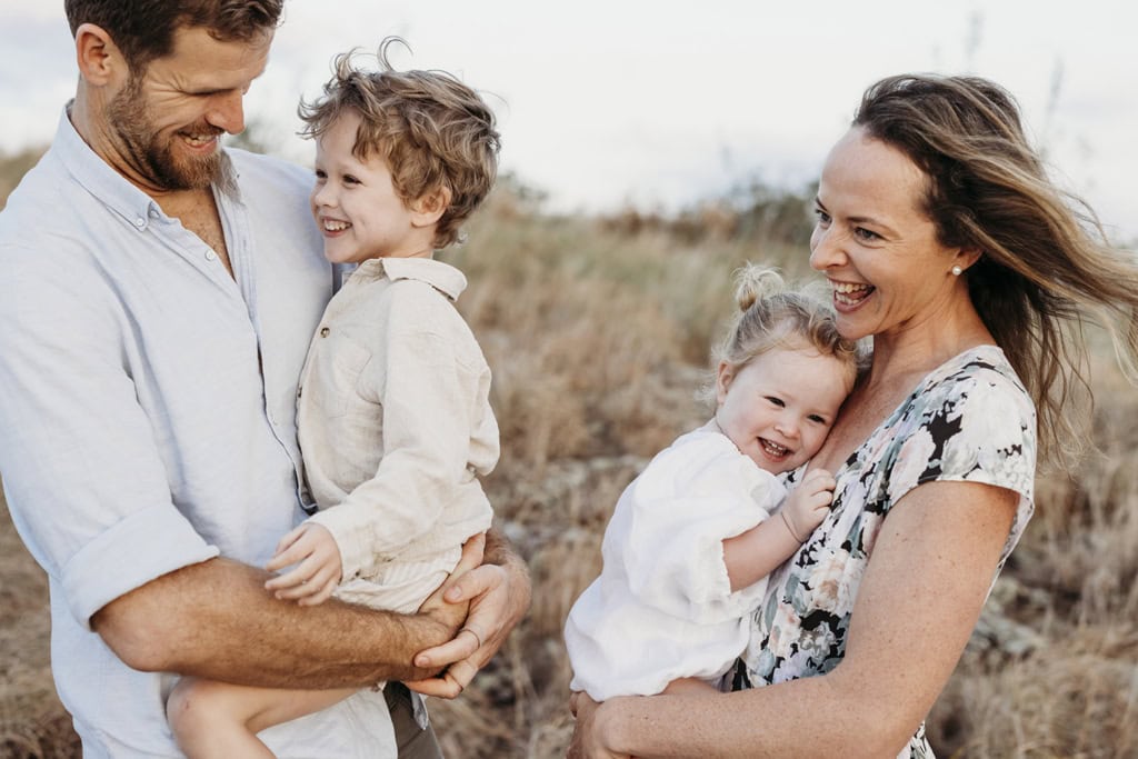 A man and woman hold their children as they laugh. 