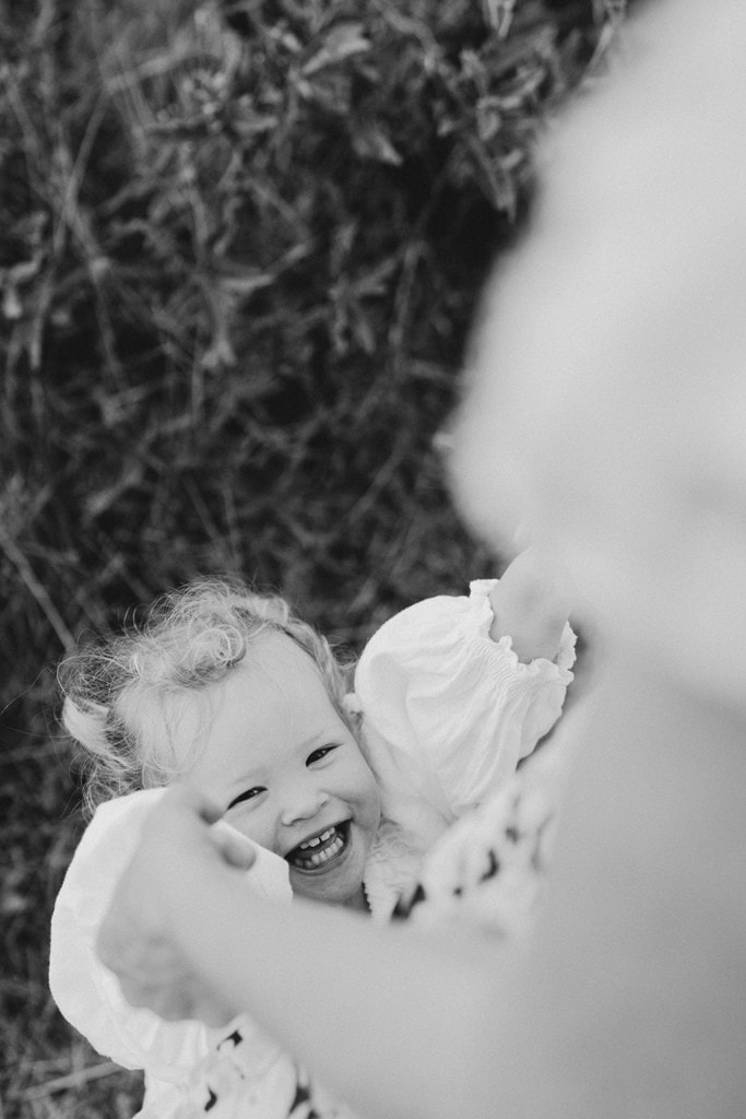 A child holds onto her mother's arms as she smiles. 