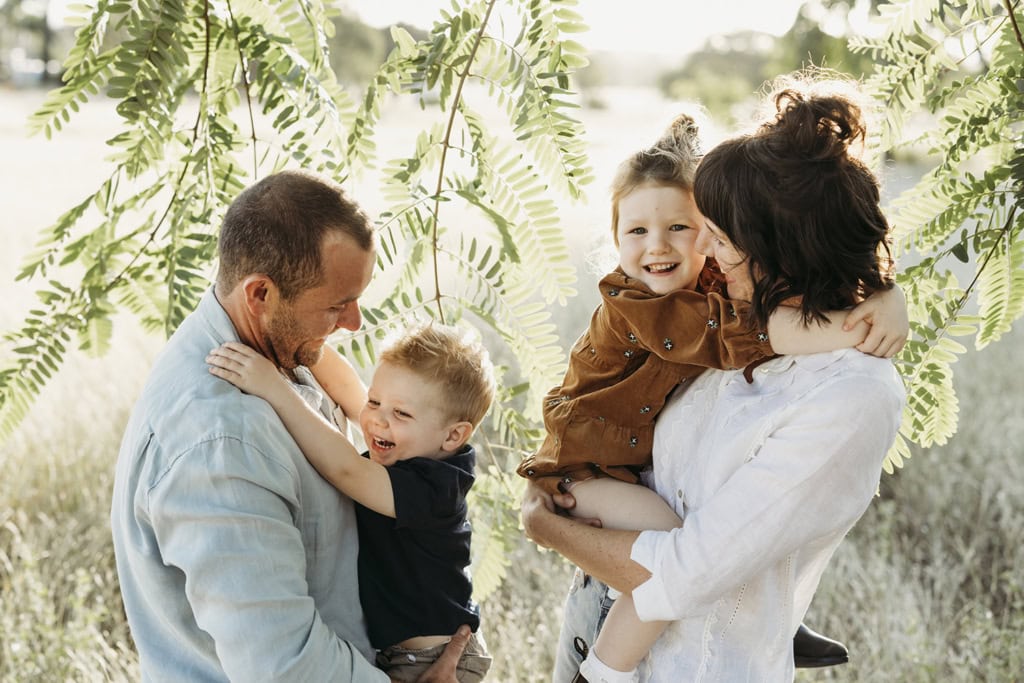 A couple hold their two small children in their arms as they all laugh.