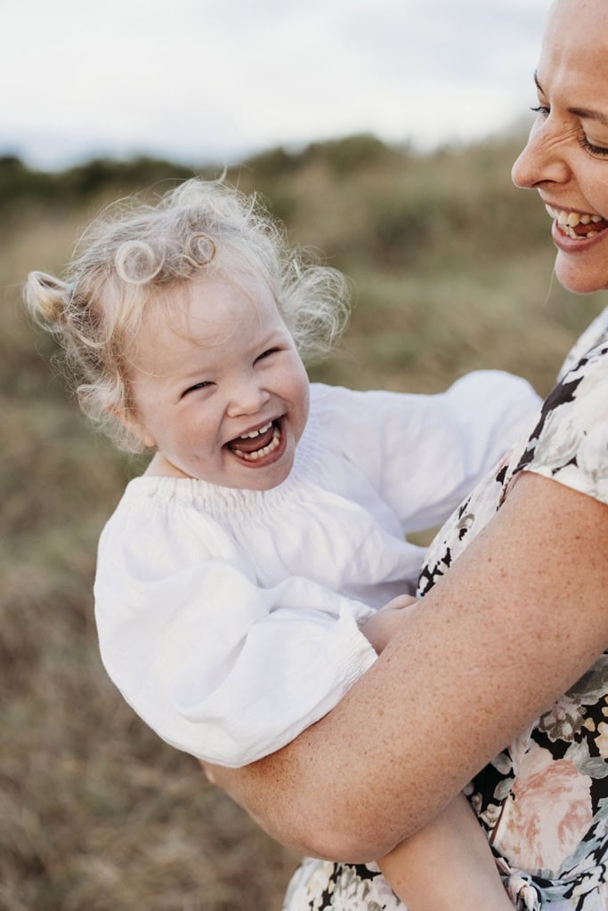 A toddler laughs as she's held in her mother's arms.